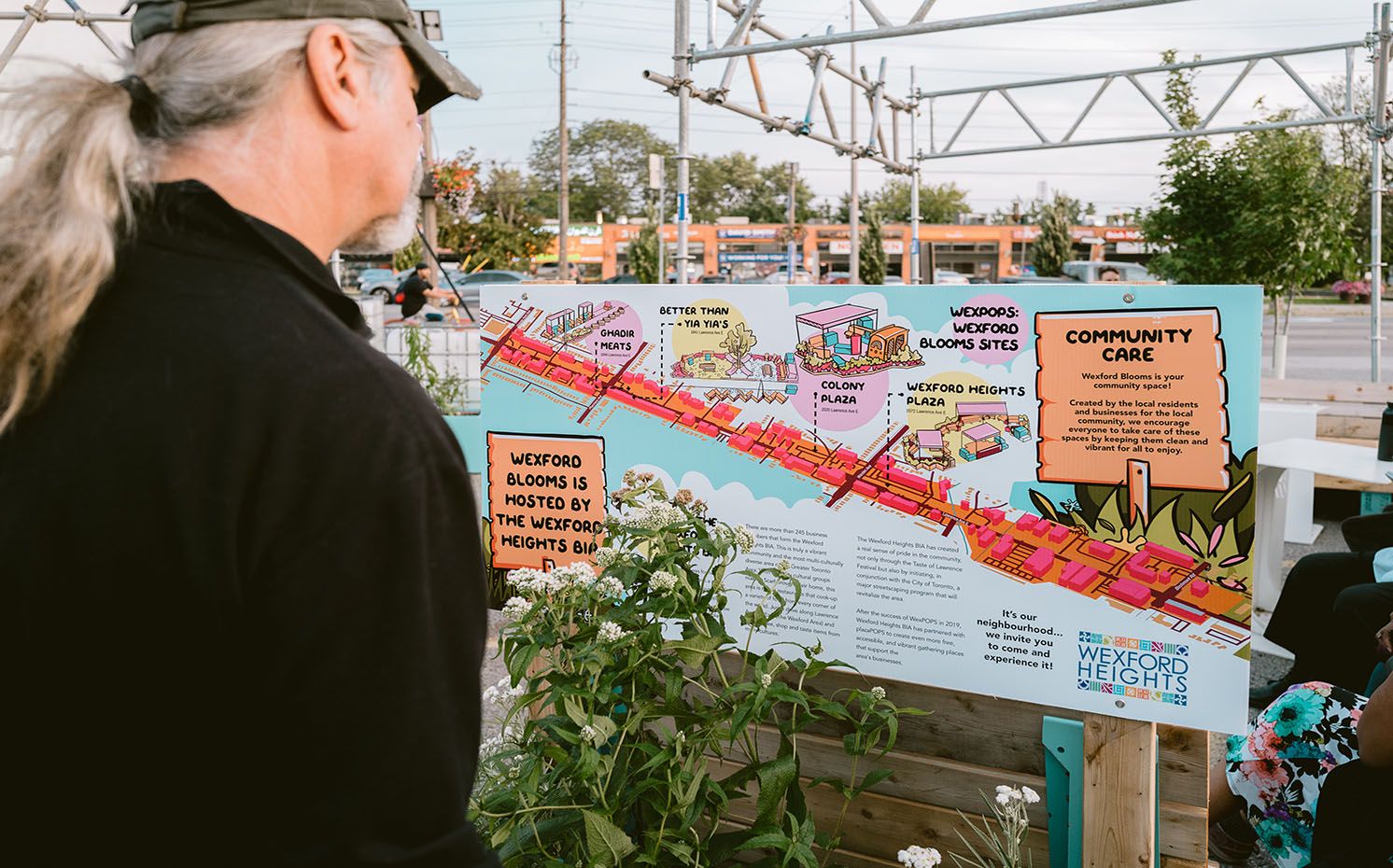Un homme aux cheveux longs et gris étudiant un panneau d'information sur le soin communautaire à Wexford Heights.