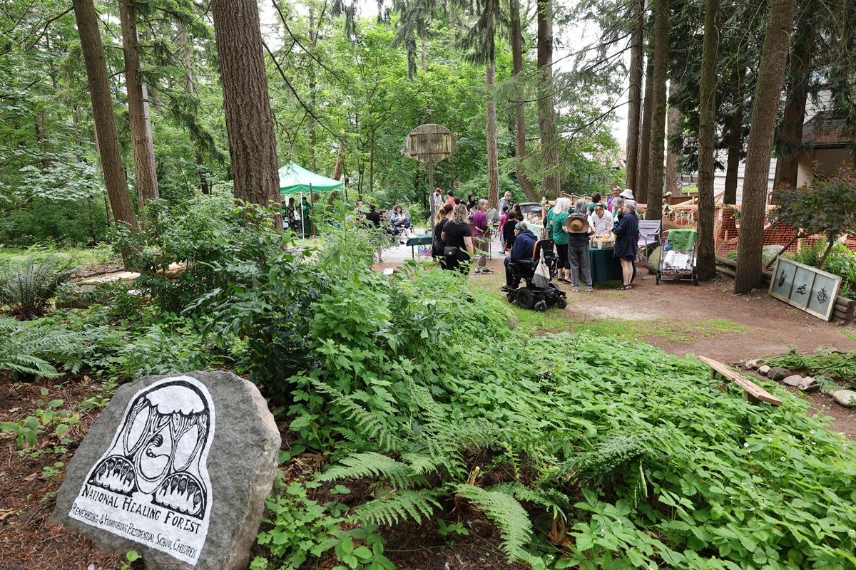 A group of people gathered for an event in a forest where we see a sign "healing forest"